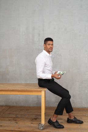 Uomo in abiti formali seduto su un tavolo e in possesso di denaro