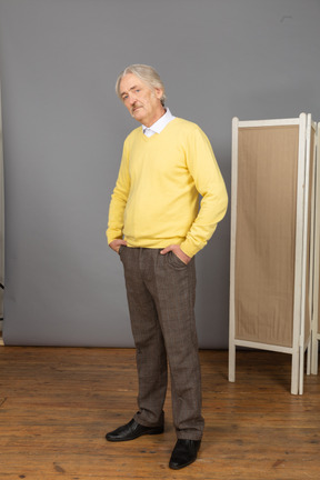 Three-quarter view of a serious old man putting hands in pockets while looking at camera