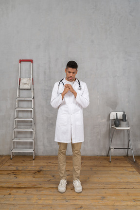 Front view of a worried young doctor standing in a room with ladder and chair