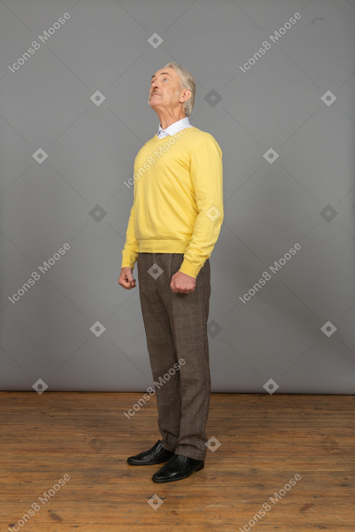 Vista de três quartos de um velho curioso em um pulôver amarelo levantando a cabeça e olhando para cima