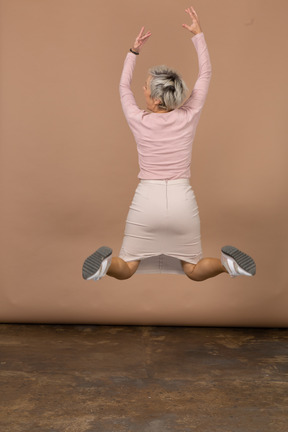 Rear view of jumping woman with raised arms