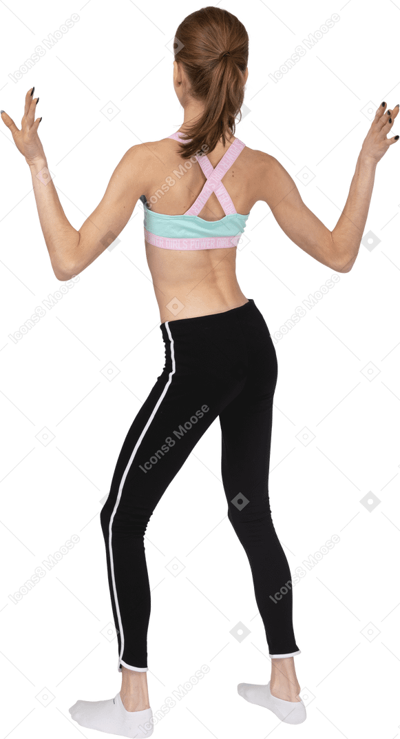 Vista posterior de una jovencita en ropa deportiva levantando las manos y bailando
