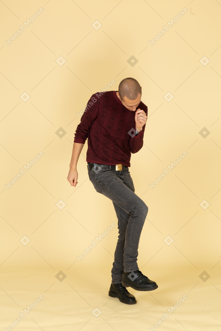 跳舞的年轻男子，穿着红色套头衫抬腿的前视图