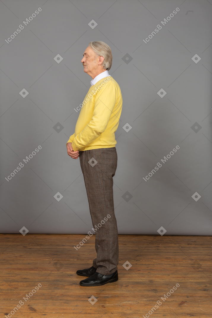 Side view of an old man in yellow pullover holding hands together with his eyes closed