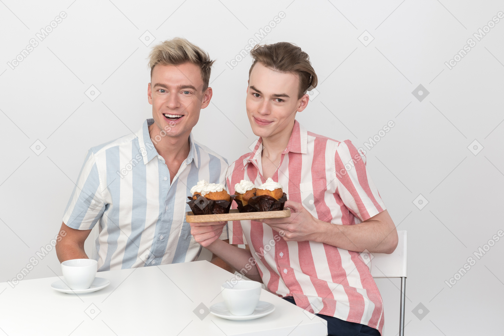 Gay couple sitting at the table and holding tray with cupcakes