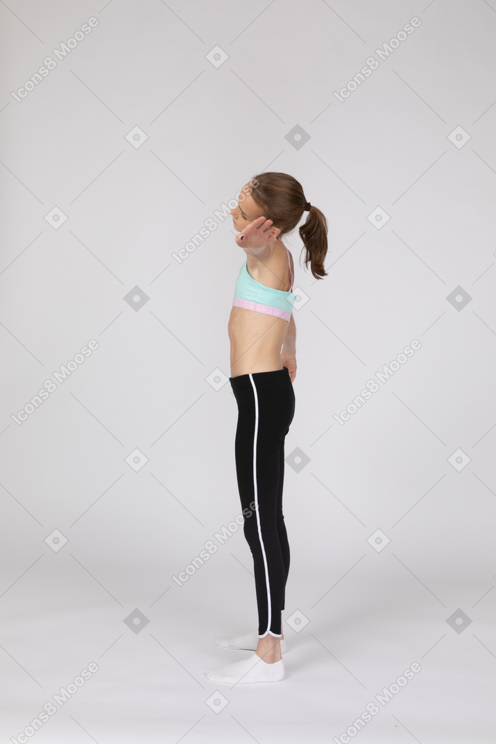 Vista lateral de uma adolescente em roupas esportivas estendendo a mão e inclinando a cabeça