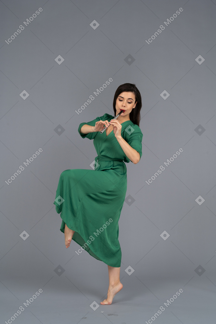 Vista lateral de una jovencita bailando en vestido verde tocando la flauta