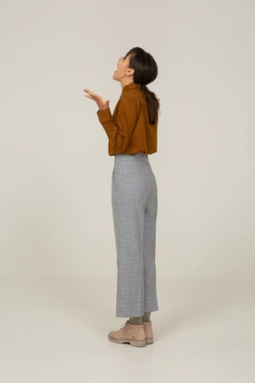 Three-quarter back view of a surprised young asian female in breeches and blouse raising hands