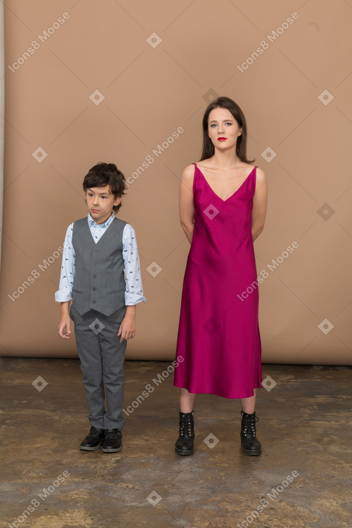 Mulher com vestido vermelho segurando os braços atrás das costas enquanto o menino está perto dela