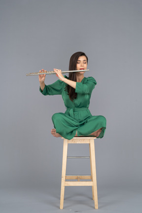 Figura intera di una giovane donna che suona il clarinetto seduta con le gambe incrociate su una sedia di legno