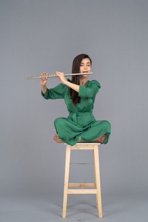 Comprimento total de uma jovem tocando clarinete sentada com as pernas cruzadas em uma cadeira de madeira