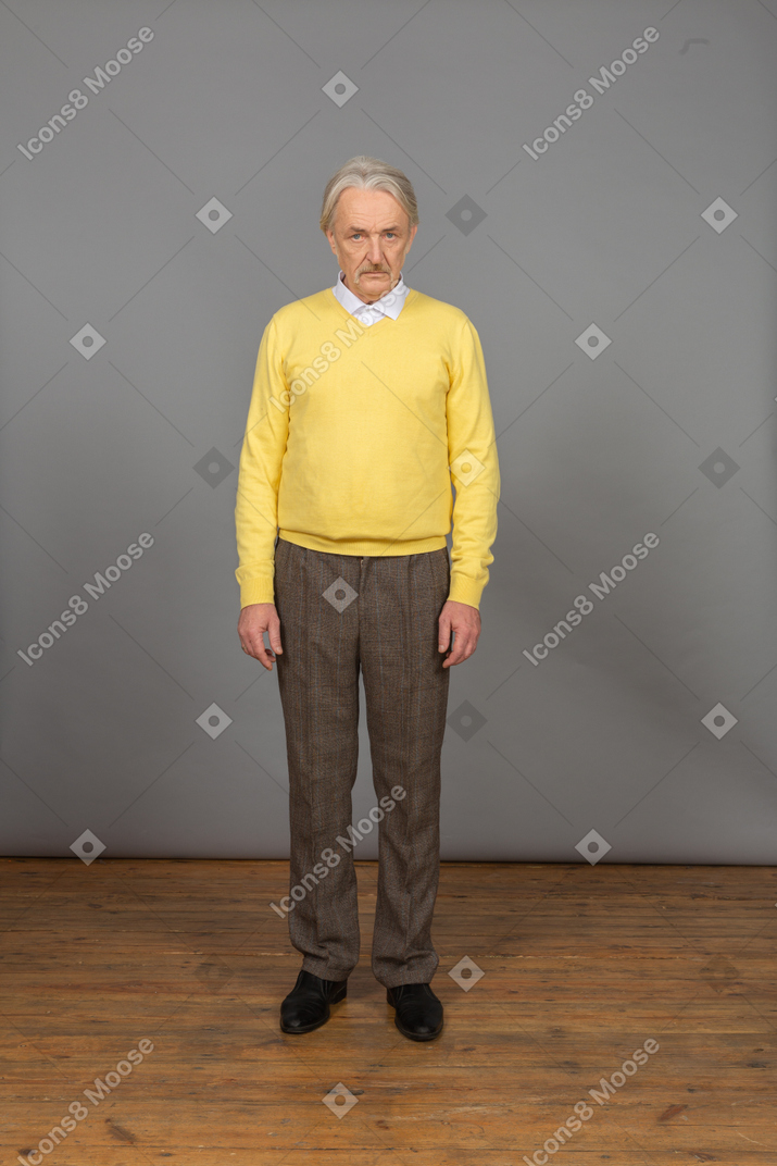 Vue de face d'un vieil homme triste en pull jaune regardant la caméra