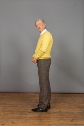 Vue latérale d'un vieil homme en pull jaune se tenant la main avec les yeux fermés