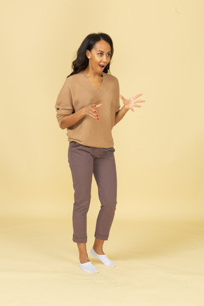 Вид в три четверти темнокожей удивленной молодой женщины, разводящей пальцы