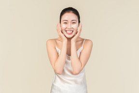 Lächelnde junge asiatische frau mit gesichtsmaske auf rührendem gesicht