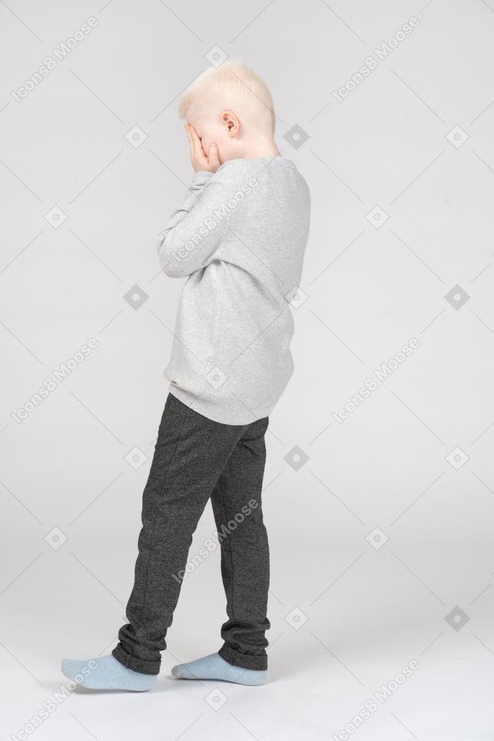 Side view of a scared boy covering his face with hands