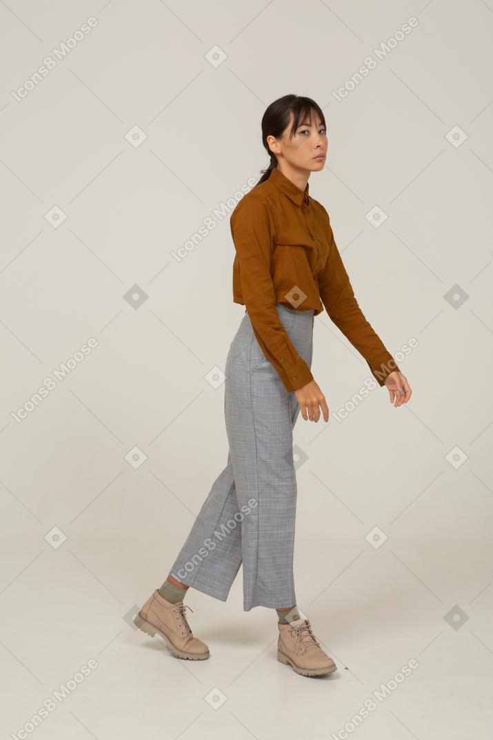 Vista di tre quarti di una giovane donna asiatica che cammina in calzoni e camicetta