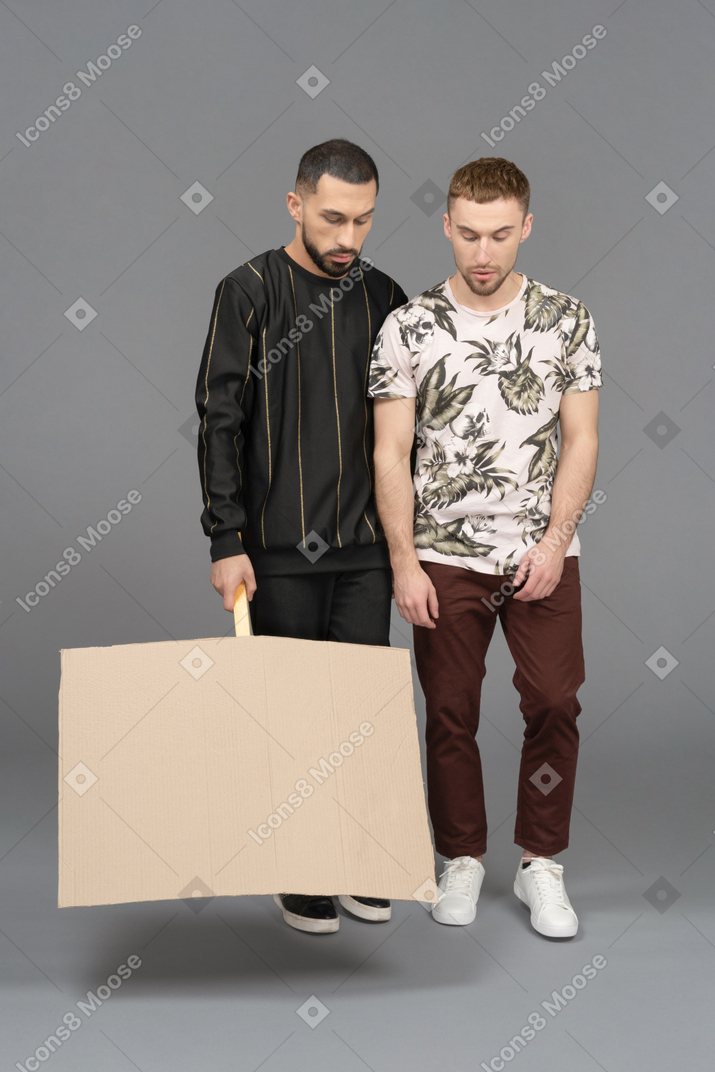 Two young men standing with lowered billboard and looking down