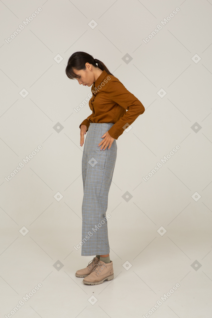 一位身着马裤和衬衫的年轻亚洲女性把手放在口袋里的侧视图