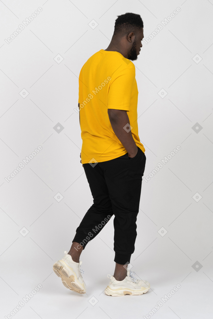 Three-quarter back view of a walking young dark-skinned man in yellow t-shirt