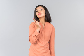 Femme indienne en haut orange tenant baume pour les lèvres et envoi air kiss