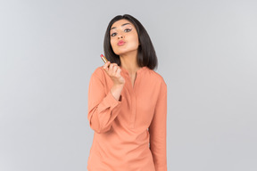 Mujer india en top naranja con bálsamo labial y enviando beso de aire