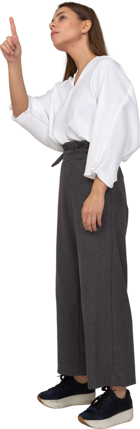 Трехчетвертный вид молодой леди в офисной одежде, указывающей пальцем вверх