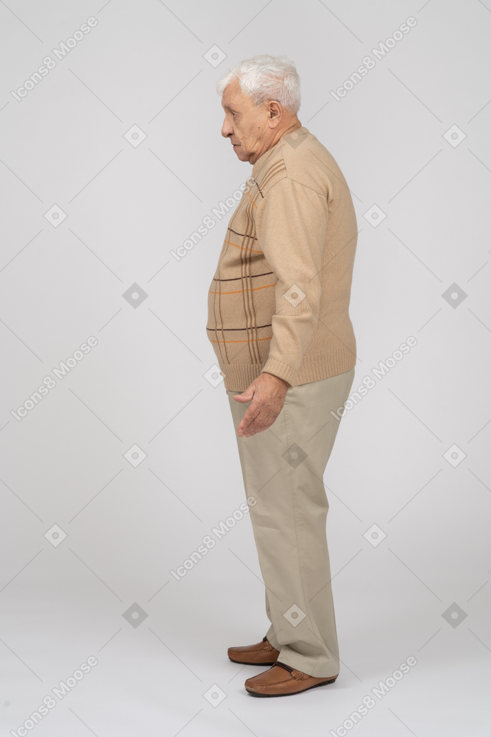 Side view of a confused old man in casual clothes standing with outstretched arms