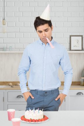 Man with party hat and horn looking at birthday cake