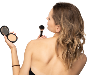 Back view of a young woman applying face powder while holding a mirror
