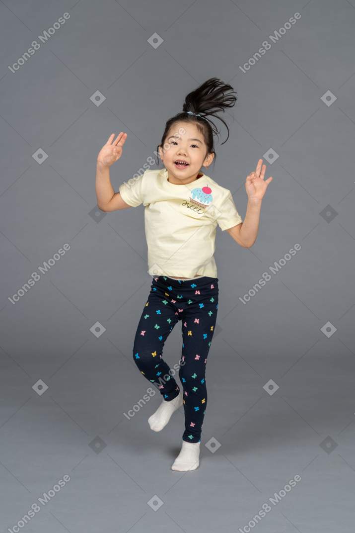 Menina pulando em uma perna com as mãos para cima