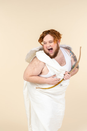 Laughing young  man dressed as a cupid holding bow