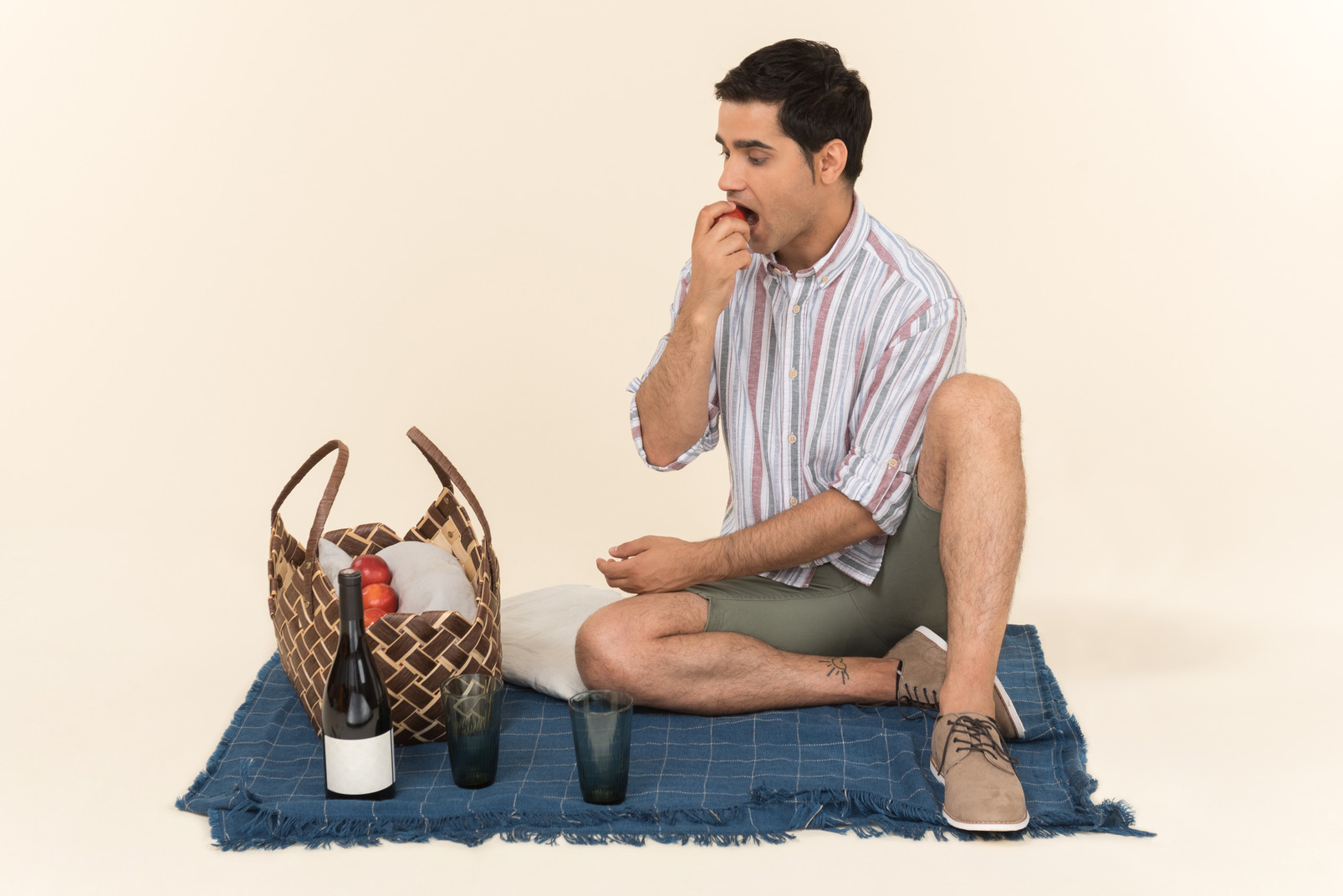 Young caucasian guy sitting on blanket and eating fruits