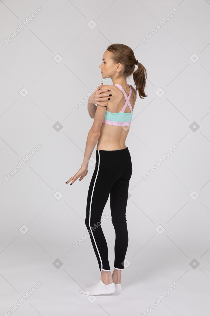 Three-quarter back view of a teen girl in sportswear touching her shoulder