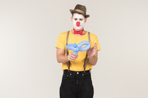 Sad looking male clown looking at balloon figure he's holding