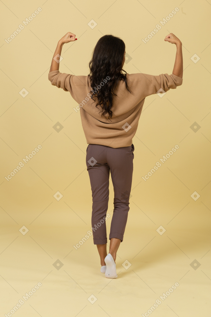 Vista posterior de una mujer joven de piel oscura levantando las manos y apretando los puños