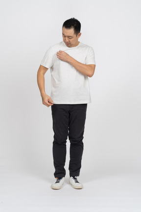 Vorderansicht eines mannes in freizeitkleidung, der auf sein t-shirt schaut