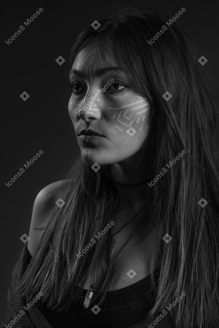 Noir three-quarter portrait of a young female with ethnic facial art looking aside