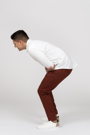 Side view of a young latino man crouching and laughing hard