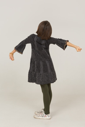 一个穿着裙子的小女孩伸展背部和手臂的四分之三后视图