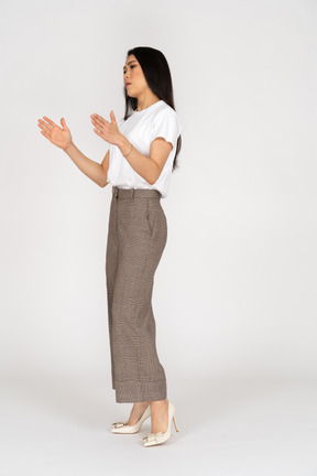 Vista di tre quarti di una giovane donna in calzoni e maglietta bianca che mostra una dimensione di qualcosa