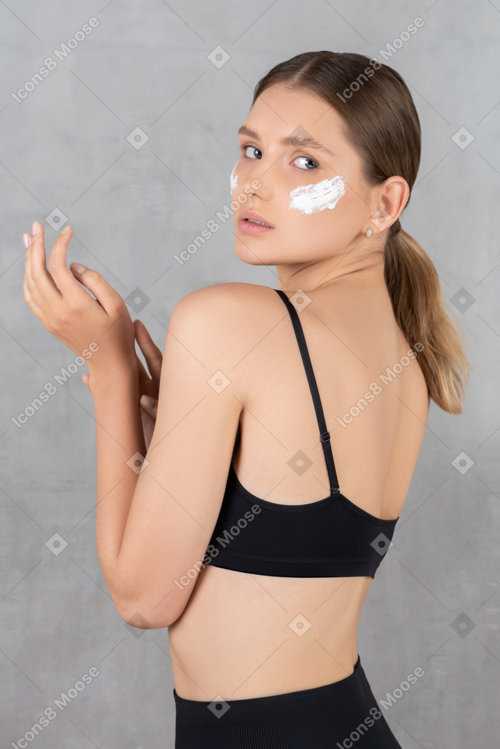 Mujer con crema en la piel mirando por encima del hombro