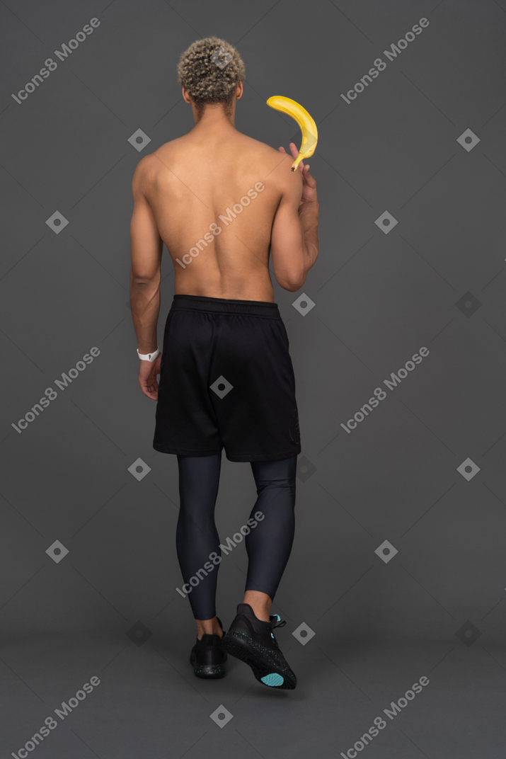 バナナを持っている若いアフロ男の背面図