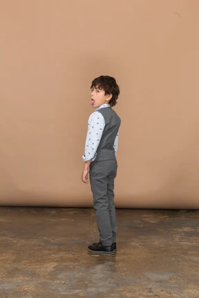 Side view of a boy in grey suit showing tongue
