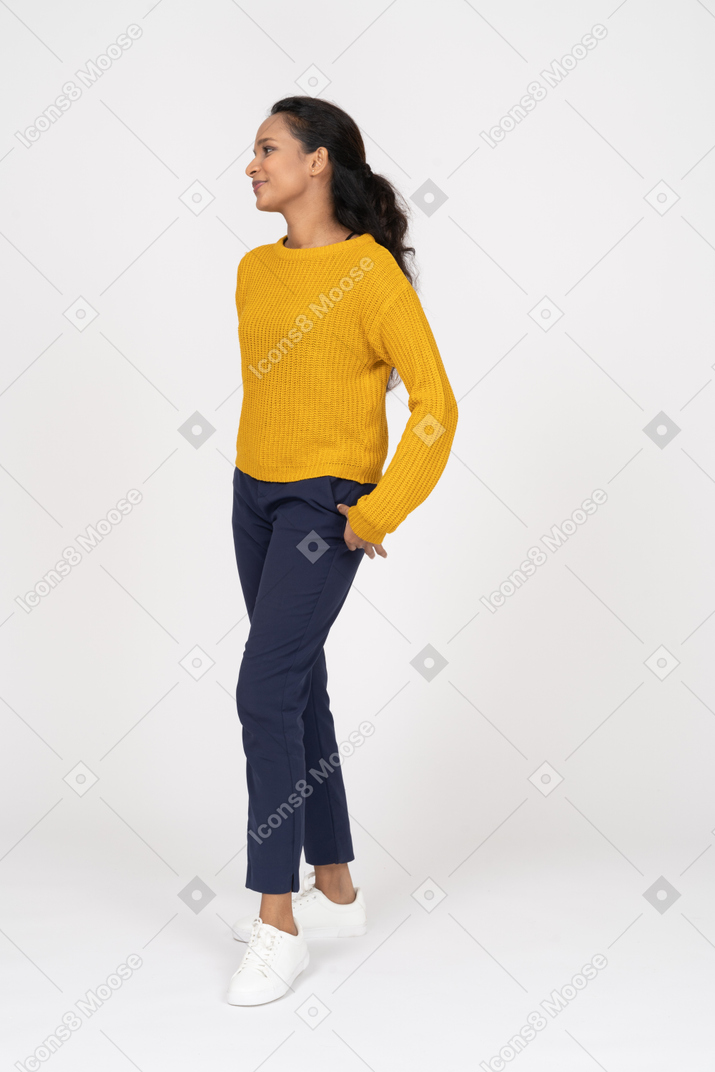 Side view of a happy girl in casual clothes posing with hands in pockets