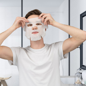 Man putting on a sheet mask in the bathroom