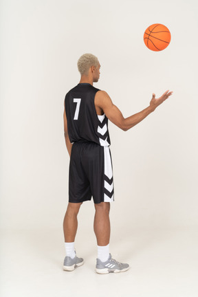 Three-quarter back view of a young male basketball player throwing a ball