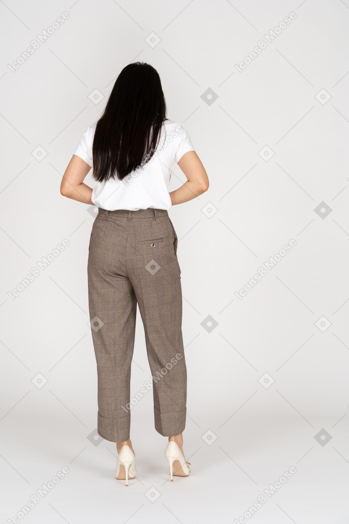 Vista de trás de uma jovem de calça e camiseta tocando seu estômago