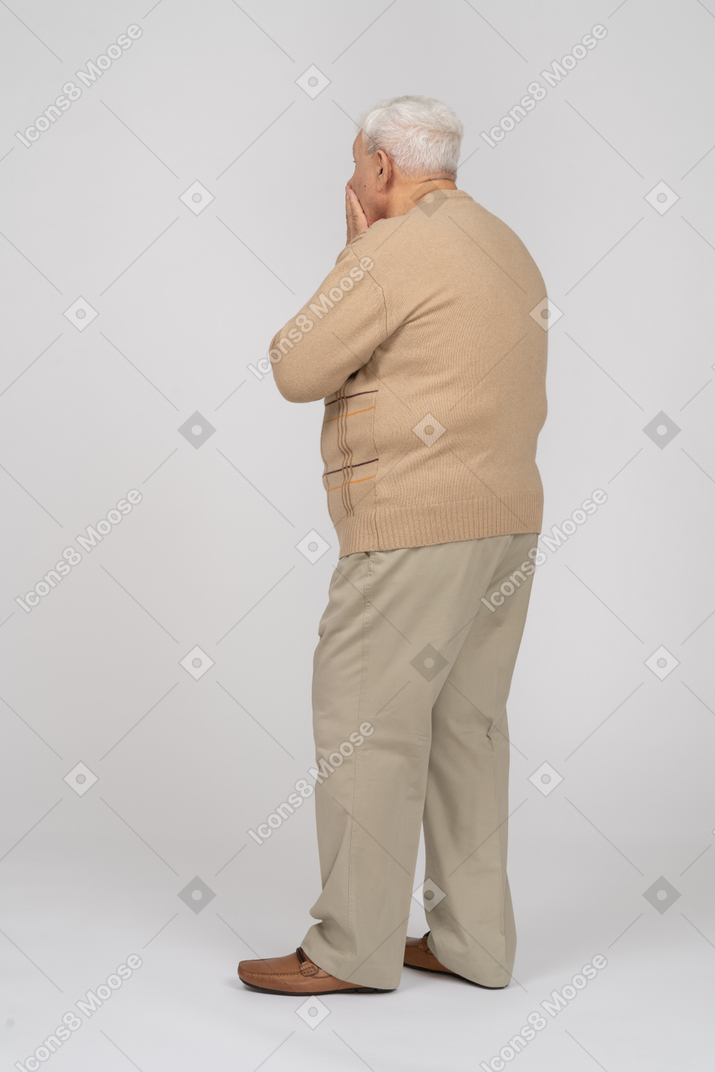 Rear view of an impressed old man in casual clothes covering mouth with hand
