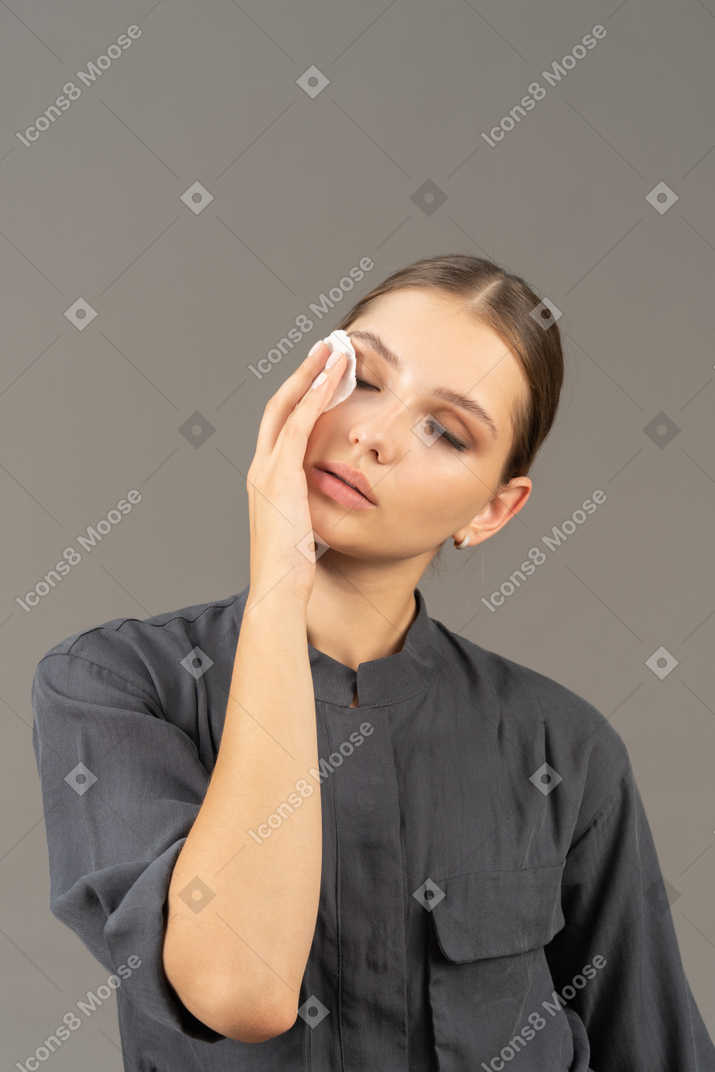 Front view of a young woman in a jumpsuit removing eye make-up